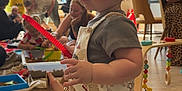 Oscar is registered to the contest to win money with this photo: toddler, child, indoor, playroom, toy, red_toy, people, adult, window, natural_light, floor, clothing, shorts, shirt, furniture, playing, group, colorful, happy, family