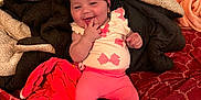 Armoni is registered to the contest to win money with this photo: baby, child, pink_clothing, headband, bow, smiling, finger_in_mouth, blanket, bed, red_bedspread, happy, indoor, cute, infant, toddler, cozy, person, soft_toys, relaxed, playful