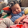 baby, sleeping, curly_hair, pigtails, blue_onesie, gray_pants, blanket, soft_toy, couch, indoor, child, peaceful, cute, infant, cozy, relaxed, portrait, home, furniture, resting