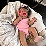 baby, pink_sunglasses, pink_outfit, blanket, baby_shoes, infant, smiling, cute, indoor, playful, child, curly_hair, accessories, relaxing, soft_texture, comfort, furniture, seat, adorable, portrait