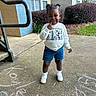 Kayleigh is registered to the contest to win money with this photo: bushes, chalk, child, concrete, cute, denim_shorts, drawing, grass, handrail, happy, outdoor, person, playful, residential_building, sidewalk, smiling, sneakers, sweatshirt, toddler, window
