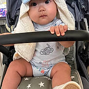 Bosco is registered to the contest to win money with this photo: baby, child, stroller, hat, towel, sitting, hand, footwear, shoe, socks, face, eyes, clothing, safety_bar, star_pattern, cute, indoors, infant, grip, adorable