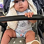baby, child, stroller, hat, towel, sitting, hand, footwear, shoe, socks, face, eyes, clothing, safety_bar, star_pattern, cute, indoors, infant, grip, adorable