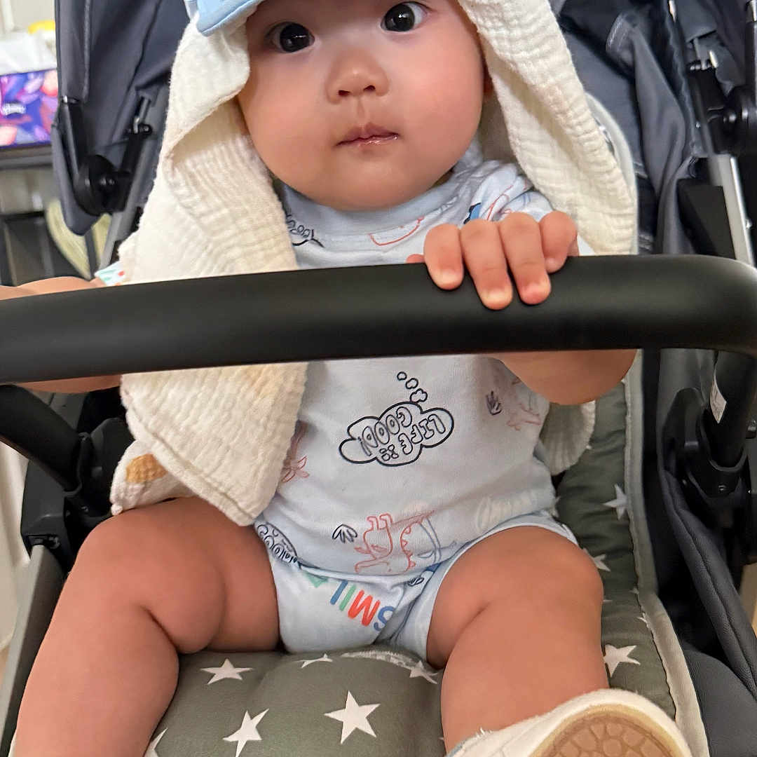 Bosco is registered to the contest to win money with this photo: adorable, baby, child, clothing, cute, eyes, face, footwear, grip, hand, hat, indoors, infant, safety_bar, shoe, sitting, socks, star_pattern, stroller, towel