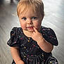 Gracelyn is registered to the contest to win money with this photo: toddler, child, baby, blue_eyes, blonde_hair, black_dress, patterned_clothing, indoor, wooden_floor, sitting, cute, curious, portrait, person, small_hand, finger_in_mouth, soft_light, puffy_sleeves, young_child, expression