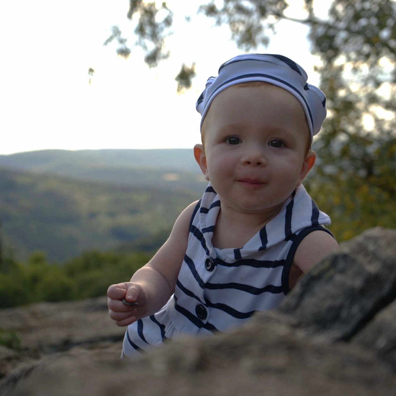 Léonïa a rejoint le concours — aidez-le/la à gagner de superbes lots ! baby, background, child, curious, cute, daylight, exploration, face, forest, hat, headwear, nature, outdoor, person, portrait, rock, scenic, smile, striped_clothing, young_child
