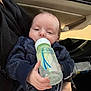 baby, infant, feeding_bottle, drinking, car_interior, car_door, seat, hand, parent_hand, jacket, clothing, face, eyes, mouth, feeding, close_up, portrait, cute, soft_lighting, relaxed