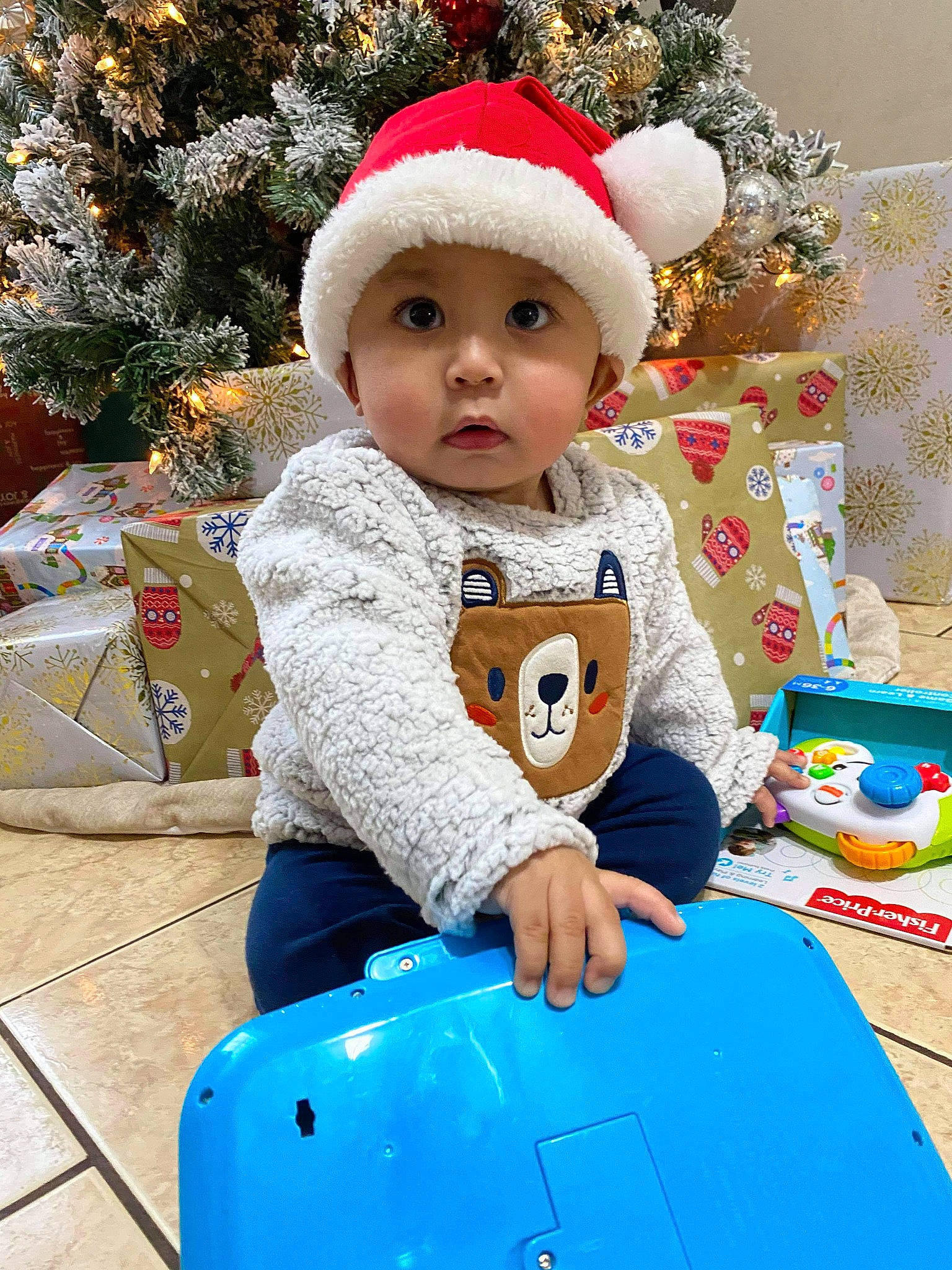 Warren is registered to the contest to win money with this photo: baby, baby_toddler_clothing, baby_toys, child, christmas, christmas_decoration, christmas_eve, christmas_ornament, christmas_tree, conifer, costume_accessory, costume_hat, fictional_character, fur, headwear, holiday, ornament, person, play, riding_toy