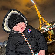 Deyton participe au concours pour gagner de l'argent avec cette photo : child, toddler, coat, beanie, hat, hood, zipped_jacket, k_way, face, cheeks, eiffel_tower, landmark, night, lights, cityscape, river, railing, winter, tourist, smile
