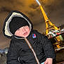 child, toddler, coat, beanie, hat, hood, zipped_jacket, k_way, face, cheeks, eiffel_tower, landmark, night, lights, cityscape, river, railing, winter, tourist, smile