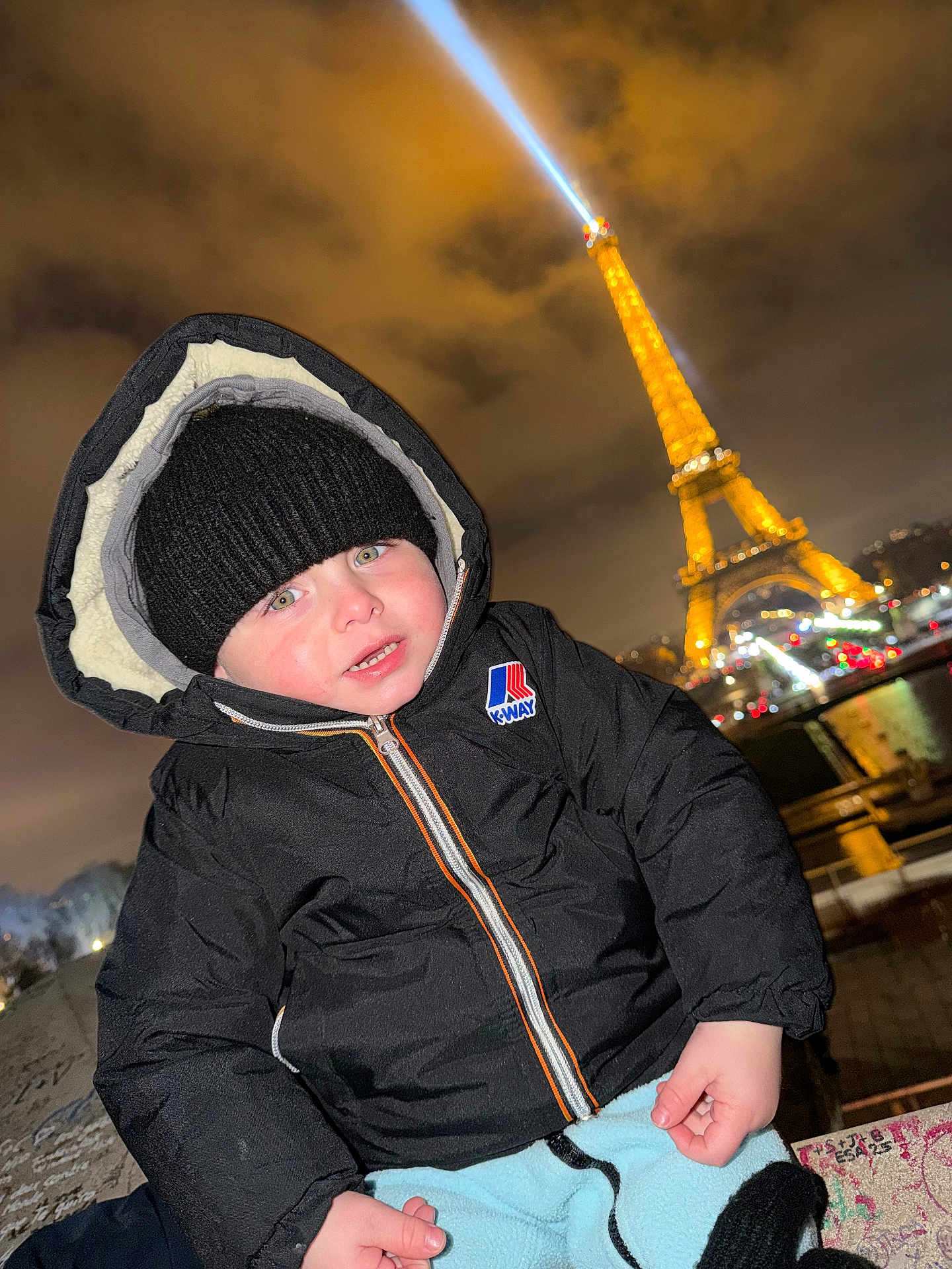 Deyton participe au concours pour gagner de l'argent avec cette photo : child, toddler, coat, beanie, hat, hood, zipped_jacket, k_way, face, cheeks, eiffel_tower, landmark, night, lights, cityscape, river, railing, winter, tourist, smile