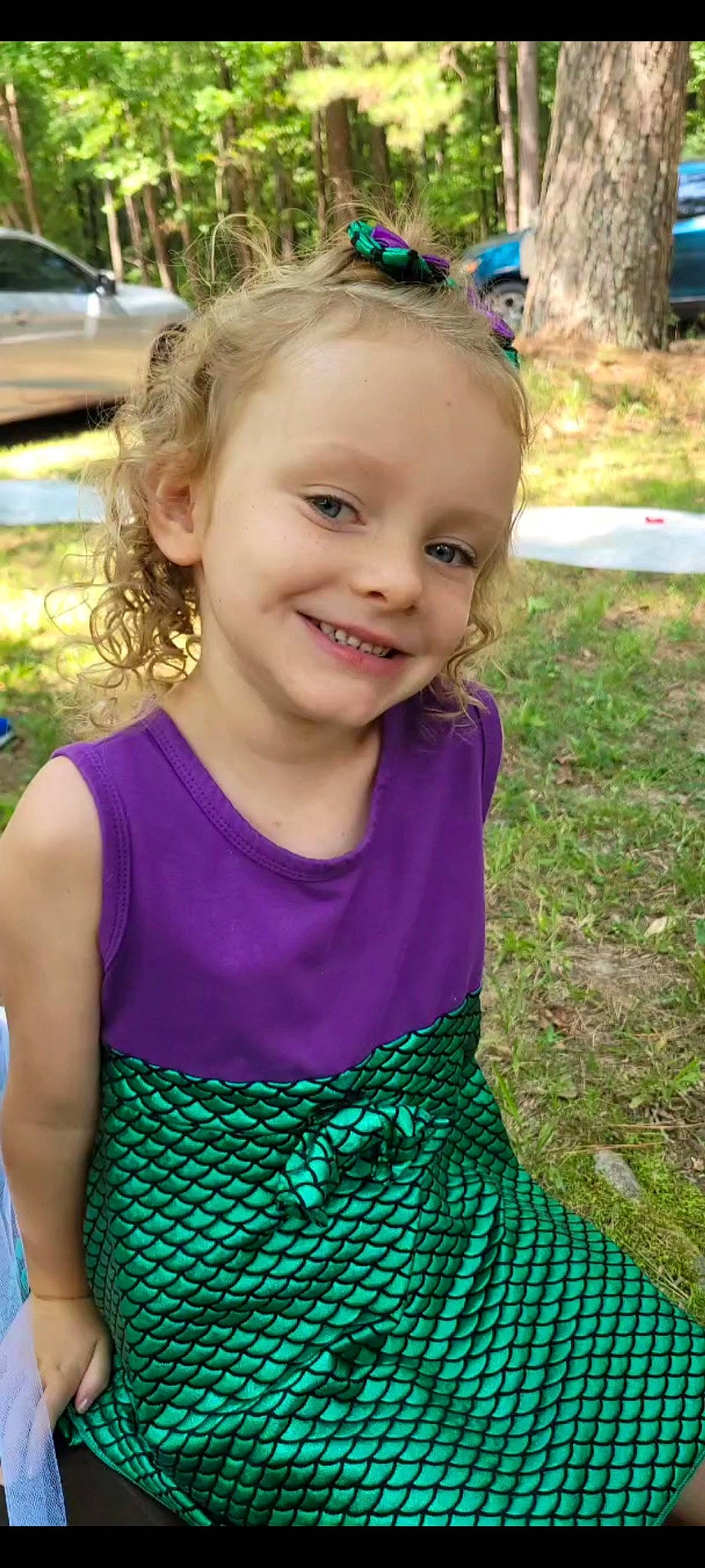 Lilly is registered to the contest to win money with this photo: baby_toddler_clothing, blue, day_dress, dress, electric_blue, face, grass, green, hair, hairstyle, happy, head, iris, joy, leaf, people_in_nature, person, pink, plant, purple