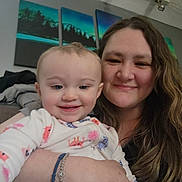 Rylee joined the competition — help win amazing prizes! baby, infant, adult, woman, mother, smiling, cuddling, selfie, portrait, family, indoor, home, cozy, long_hair, floral_clothing, baby_clothes, wall_art, seated, happy, photograph