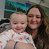 adult, baby, baby_clothes, cozy, cuddling, family, floral_clothing, happy, home, indoor, infant, long_hair, mother, photograph, portrait, seated, selfie, smiling, wall_art, woman