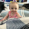 Rylee is registered to the contest to win money with this photo: baby, child, infant, smiling, happy, portrait, face, eyes, pink_clothing, sitting, indoors, living_room, blanket, striped_blanket, toy, toy_storage, furniture, carpet, basket, home