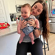 Sierra is registered to the contest to win money with this photo: baby, woman, kitchen, smile, holding, happy, person, long_hair, infant, casual_clothing, countertop, stool, refrigerator, indoor, family, portrait, home, cabinet, floor, appliance