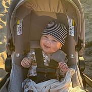 Liam joined the competition — help win amazing prizes! baby, smiling, stroller, beach, sand, blanket, hat, onesie, child, sunlight, outdoor, happy, infant, seatbelt, cozy, cushion, portrait, cute, sunny, warm