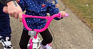 Kylie Rose joined the competition — help win amazing prizes! child, girl, bicycle, pink_bike, pigtails, adult_hand, outdoor, sidewalk, casual_clothing, footwear, support, learning, play, parked_car, background, daylight, determined, person, two_children, road