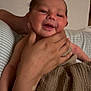 baby, newborn, infant, hand, person, blanket, smile, face, indoor, home, adult_hand, skin, comfort, cozy, resting, young_child, portrait, soft_light, couch, striped_pillow