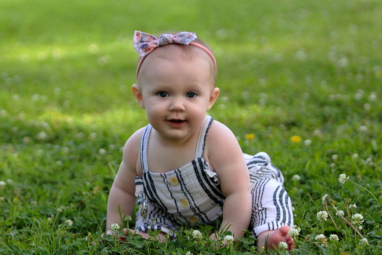 Sawyer is registered to the contest to win money with this photo: baby, baby_toddler_clothing, botany, dress, facial_expression, flower, grass, grass_family, grassland, groundcover, happy, leaf, meadow, natural_environment, people_in_nature, person, plant, smile, summer, sunlight