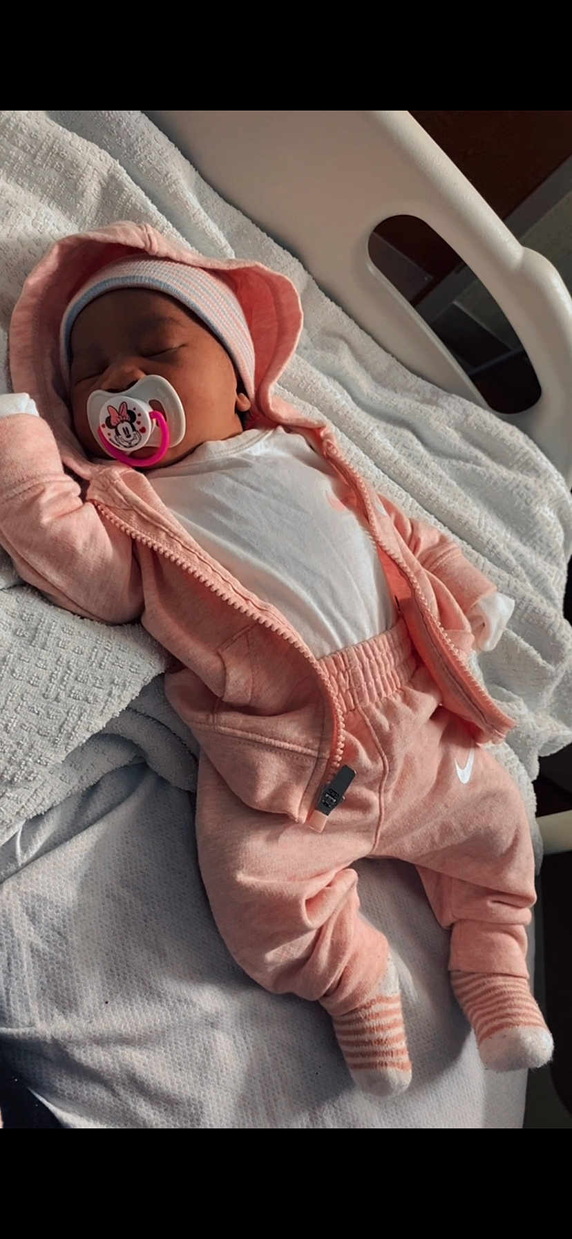 Naiari is registered to the contest to win money with this photo: baby, blanket, child, cozy, cute, hat, hoodie, hospital_bed, indoors, infant, newborn, pacifier, pajamas, pink_clothing, relaxing, sleep, sleeping, soft_light, striped_socks, white_clothing