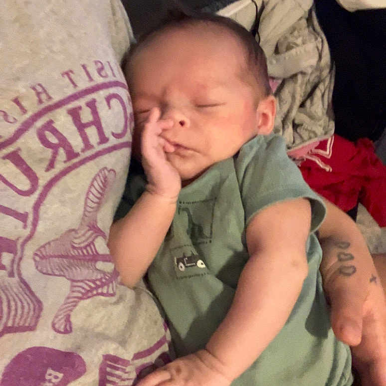 Miles Young joined the competition — help win amazing prizes! baby, infant, sleeping, child, portrait, close_up, indoors, blanket, onesie, green_clothing, adult, parent, hand, cheek, cozy, resting, bed, home, candid, family