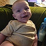 baby, smile, infant, couch, green_couch, bottle, milk_bottle, crate, purple_crate, beige_clothing, ribbed_clothing, happy, indoors, person, child, face, seated, baby_bottle, cozy, home