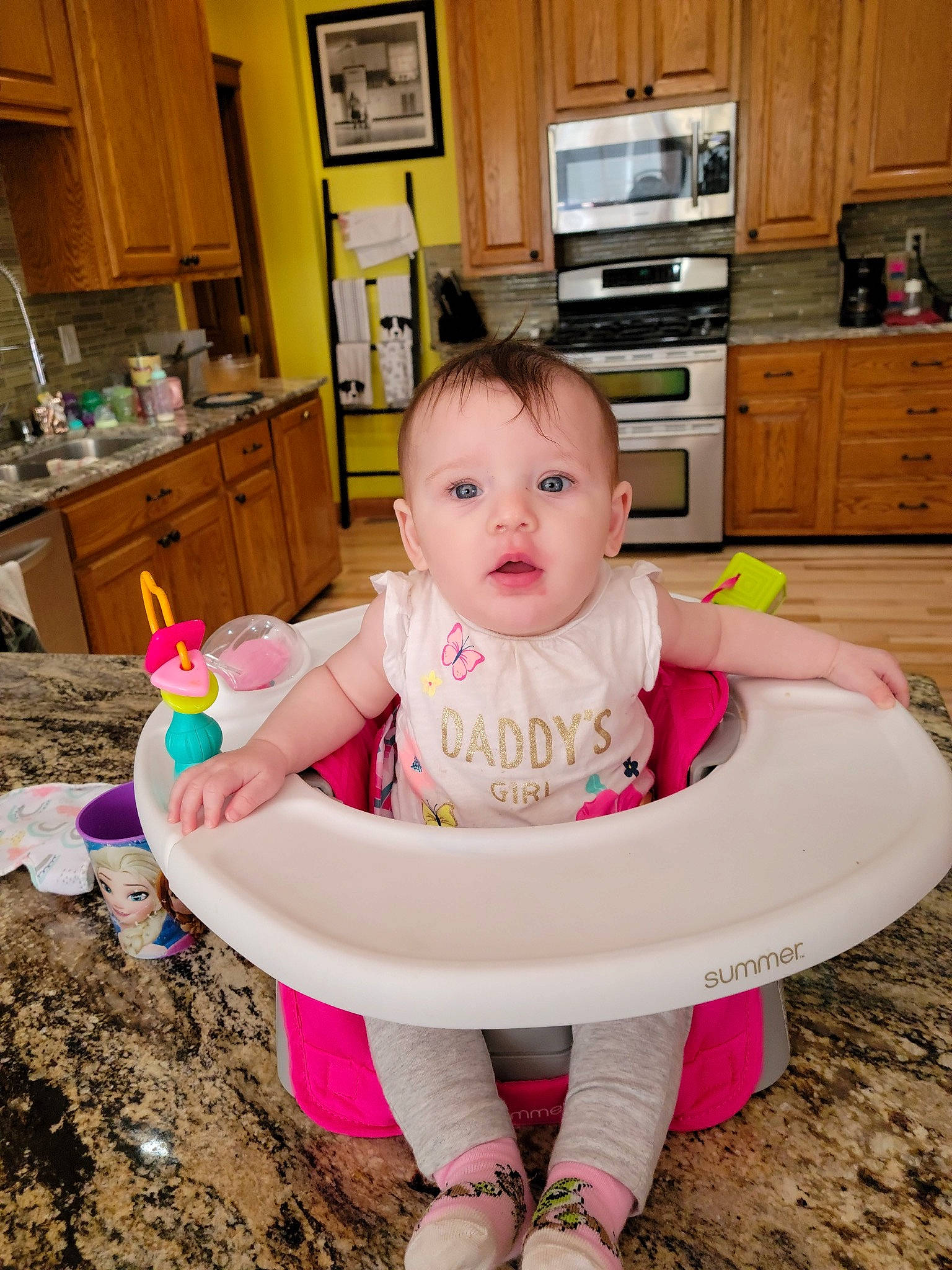 Alivia is registered to the contest to win money with this photo: baby, baby_products, baby_toddler_clothing, cabinetry, child, cupboard, drawer, happy, home_appliance, kitchen, kitchen_appliance, microwave_oven, person, picture_frame, pink, room, surprise, t_shirt, tableware, television