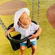 Ilyass a rejoint le concours — aidez-le/la à gagner de superbes lots ! toddler, swing, playground, child, hat, white_shirt, shorts, barefoot, chains, yellow_surface, looking_up, outdoor, sunlight, curious, baby_swing, play_area, childrens_clothing, summer, safety_seat, bright_eyes