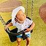 toddler, swing, playground, child, hat, white_shirt, shorts, barefoot, chains, yellow_surface, looking_up, outdoor, sunlight, curious, baby_swing, play_area, childrens_clothing, summer, safety_seat, bright_eyes