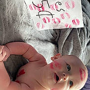 Miles is registered to the contest to win money with this photo: baby, infant, lipstick, kiss_marks, diaper, blanket, paper, handwriting, red_color, face_paint, child, cute, smiling, skin, lying_down, soft_texture, playful, expression, indoors, person