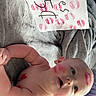baby, blanket, child, cute, diaper, expression, face_paint, handwriting, indoors, infant, kiss_marks, lipstick, lying_down, paper, person, playful, red_color, skin, smiling, soft_texture