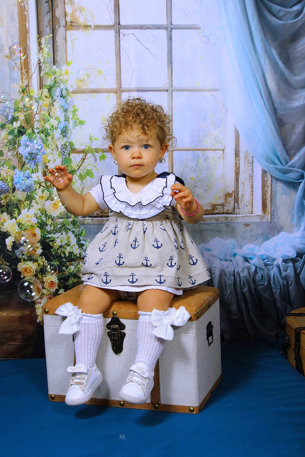 ève Horn participe au concours pour gagner de l'argent avec cette photo : child, toddler, curly_hair, blue_eyes, dress, anchors, socks, bows, shoes, trunk, window, flowers, bubbles, curtains, blue, indoor, portrait, cute, sitting, playful