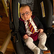 Lucas is registered to the contest to win money with this photo: baby, child, car_seat, glasses, tie, clothing, indoor, person, infant, cute, serious, fashion, seat, footwear, socks, portrait, young, adorable, small, seated