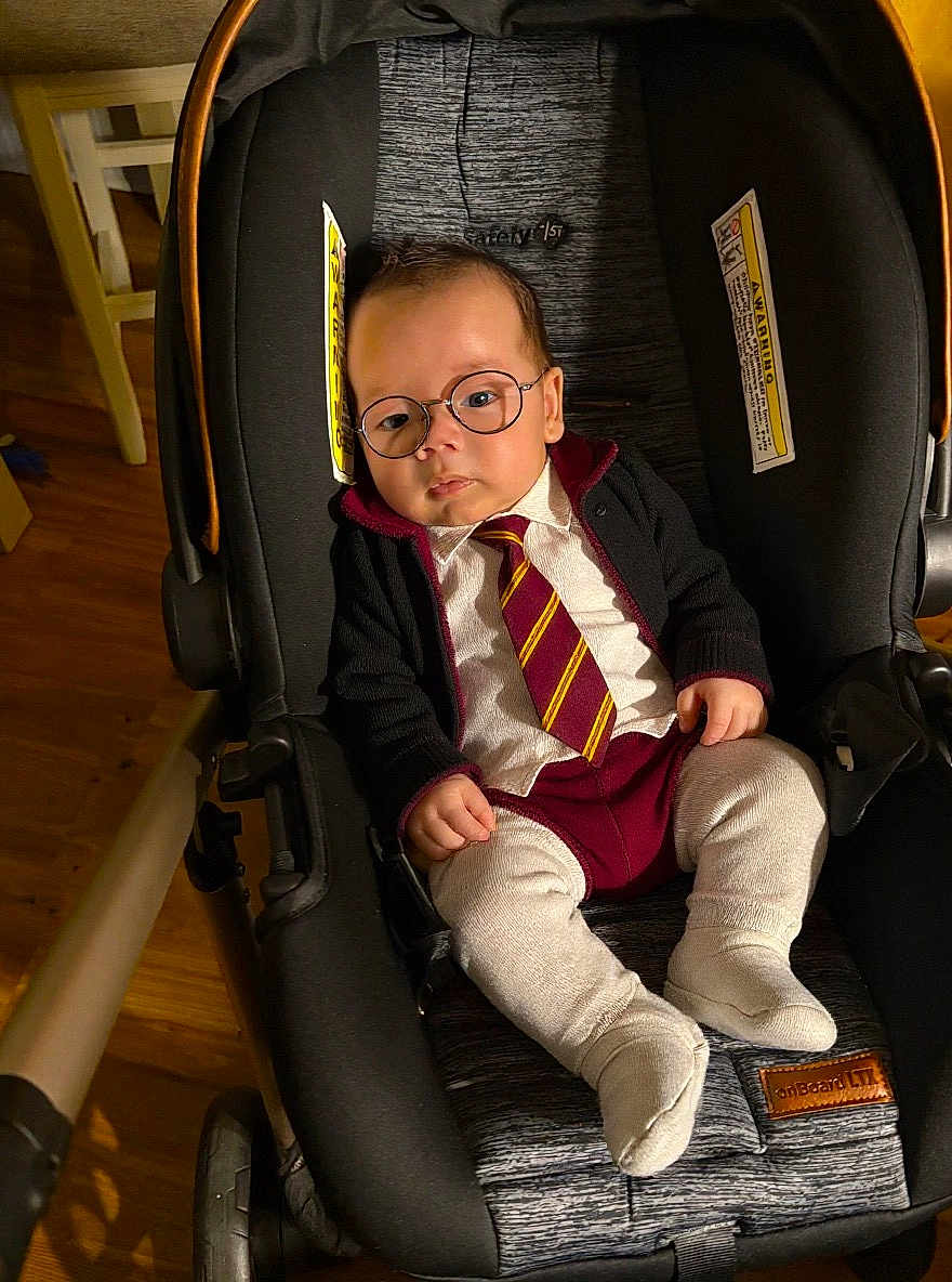 Lucas is registered to the contest to win money with this photo: baby, child, car_seat, glasses, tie, clothing, indoor, person, infant, cute, serious, fashion, seat, footwear, socks, portrait, young, adorable, small, seated