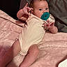baby, infant, child, portrait, lying_down, pacifier, pink_blanket, onesie, bed, indoor, face, eyes, hand_gesture, smiling, baby_clothing, soft_blanket, nursery, close_up, photography, adorable