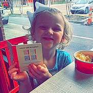 Gracelyn is registered to the contest to win money with this photo: architecture, building, child, city, cutlery, face, female, food, girl, head, lunch, meal, person, photography, portrait, road, spoon, street, text, urban