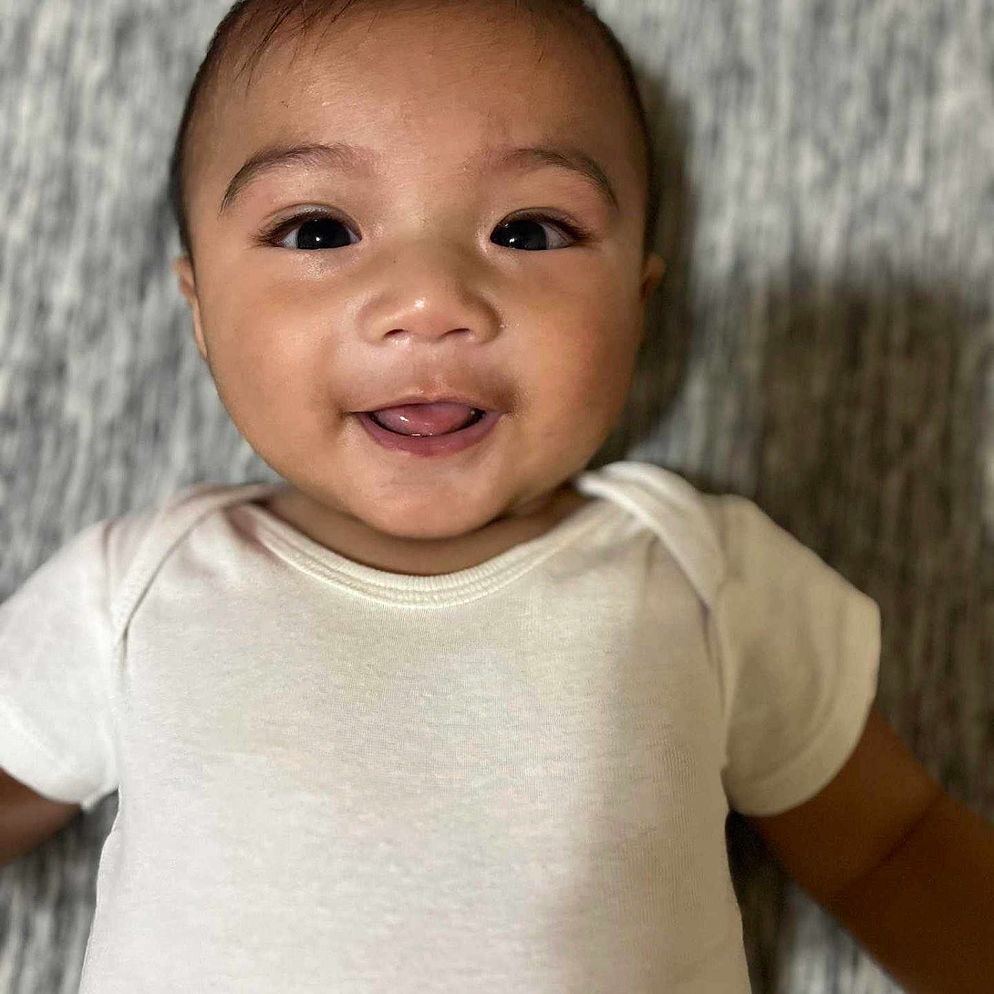 Nayahn joined the competition — help win amazing prizes! baby, cheeks, child, closeup, cute, expression, eyes, face, happy, head, indoor, infant, lying_down, person, portrait, skin, smile, soft_texture, tongue, white_onesie