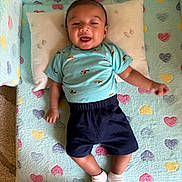 Nayahn joined the competition — help win amazing prizes! baby, child, smiling, lying_down, pillow, blanket, heart_pattern, blue_shirt, shorts, socks, indoors, cute, happy, person, infant, cozy, soft, playful, young, resting