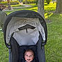 baby, stroller, smiling, child, outdoor, park, grass, trees, sunlight, happy, infant, nature, seatbelt, canopy, person, recreation, daytime, playground, bench, picnic