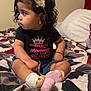 bedroom, bedspread, black_shirt, bracelet, child, cross_legged, curly_hair, cute, earrings, expression, girl, headband, indoor, pink, portrait, shirt, sitting, socks, text_on_clothing, toddler