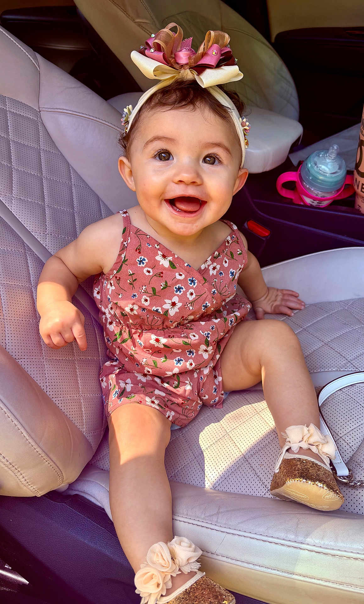 Azalea is registered to the contest to win money with this photo: baby, child, smiling, car_seat, headband, dress, footwear, flower_pattern, happy, sitting, infant, cute, indoors, leather_seat, accessory, portrait, one_person, baby_shoes, car_interior, young_child