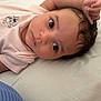baby, infant, face, eyes, pink_shirt, cartoon, lying_down, bed, white_bed_sheet, hand, curly_hair, skin, child, portrait, closeup, cute, young, person, indoors, expression