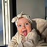 baby, child, face, blue_eyes, headband, tongue_out, cozy, knit_sweater, smiling, cute, indoor, natural_light, playful, person, portrait, infant, expression, window, warm_light, happy