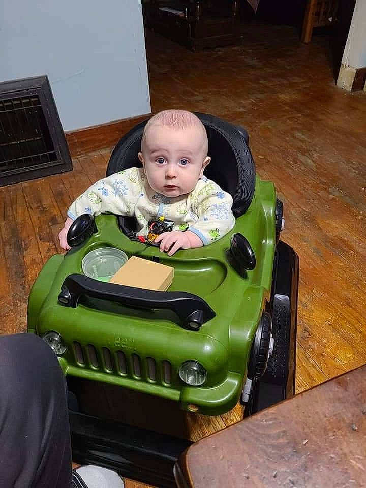 Evander is registered to the contest to win money with this photo: automotive_design, baby, baby_toddler_clothing, bumper, child, floor, flooring, green, hardwood, machine, person, play, riding_toy, sitting, t_shirt, toddler, toy, toy_vehicle, varnish, wood