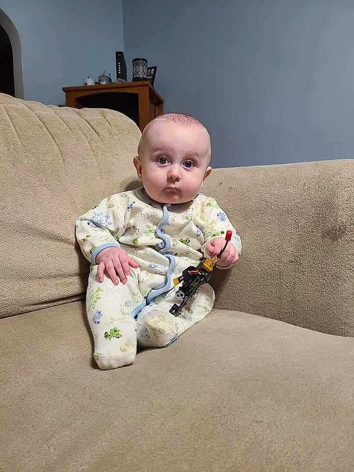 Evander is registered to the contest to win money with this photo: ankle, baby, baby_toddler_clothing, cheek, comfort, couch, foot, human_body, lamp, living_room, mouth, nightwear, nose, person, pillow, sitting, slipcover, sock, sofa_bed, throw_pillow