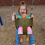 Scarlett joined the competition — help win amazing prizes! toddler, child, swing, playground, doll, toy, happy, smiling, outdoor, woodchips, brick_wall, casual_clothing, sneakers, blue_jeans, green_shirt, playtime, person, young_child, daylight, fun