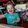 Scarlett is registered to the contest to win money with this photo: toddler, child, smiling, happy, crayons, coloring_sheet, table, restaurant, indoor, person, hair_tie, teeth, clothing, face, portrait, sitting, fun, cute, bright_colors, casual