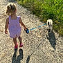 back_view, child, dog, field, grass, greenery, leash, nature, outdoor, path, pet, retractable_leash, romper, sandals, shadow, small_dog, summer, sunlight, toddler, walking
