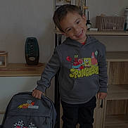Naël a rejoint le concours — aidez-le/la à gagner de superbes lots ! child, smiling, hoodie, spongebob, backpack, cars, lightning_mcqueen, shoes, indoor, mirror, shelf, wooden_furniture, toy, person, happy, standing, casual_clothing, young_boy, black_pants, colorful_clothing